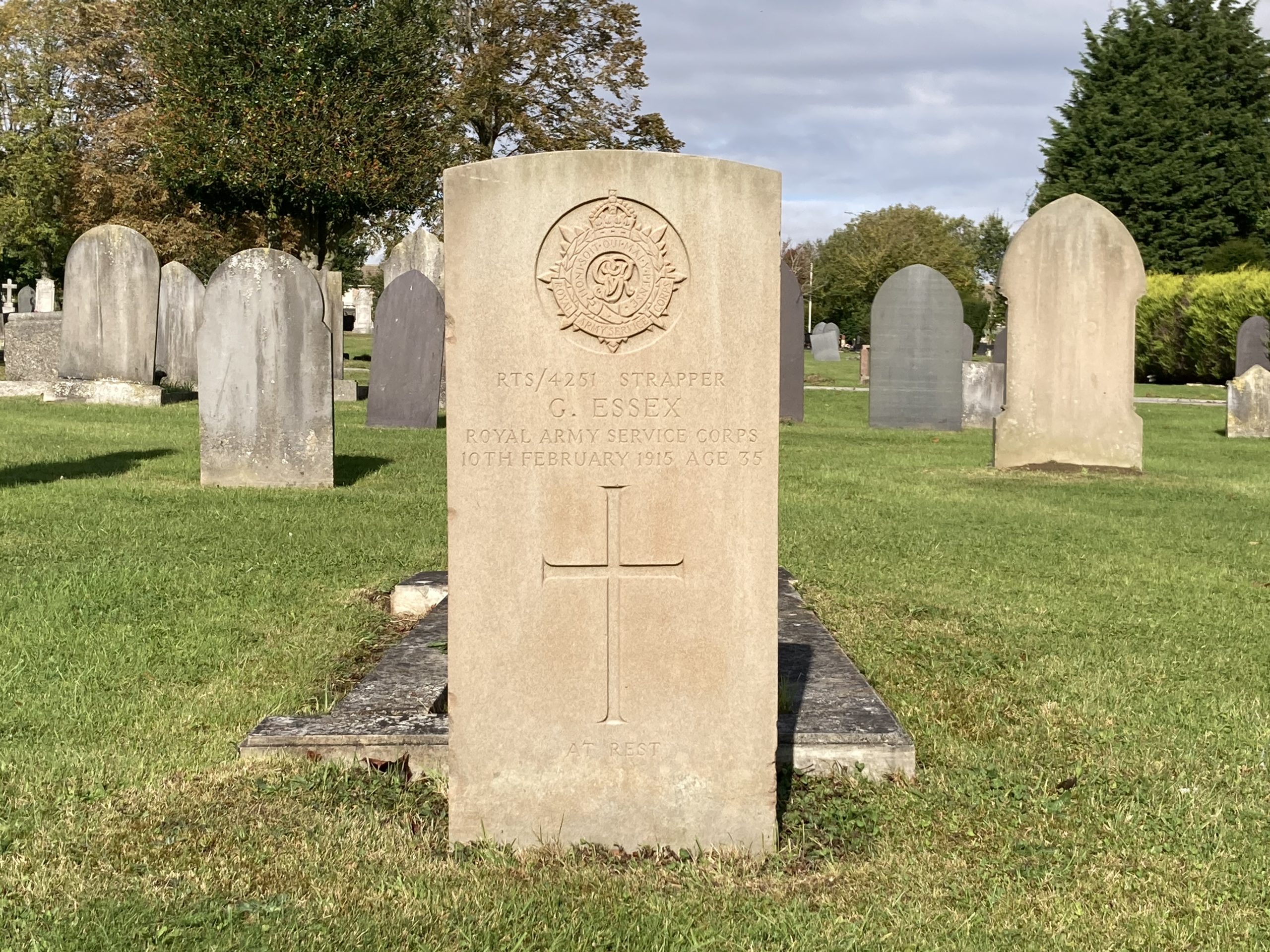 Focuses on one headstone which is in a plot of green grass. You can see other headstones in the background